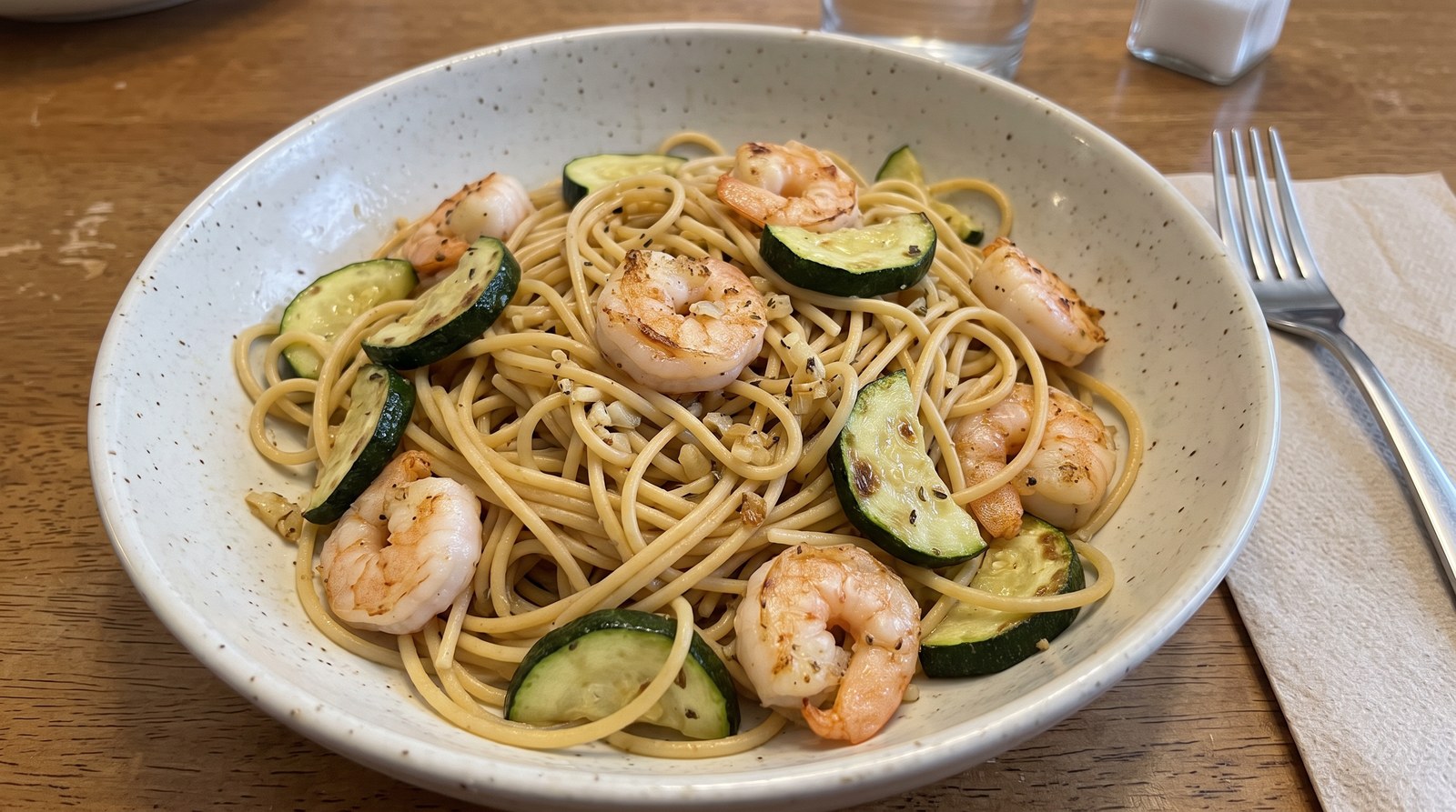 Garlic-lemon shrimp and zucchini half-moons tossed with protein spaghetti in a shallow white bowl