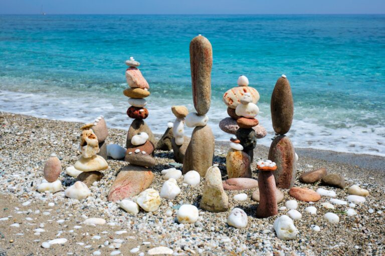 Balanced pebble stone stacks on a beach beside blue water.