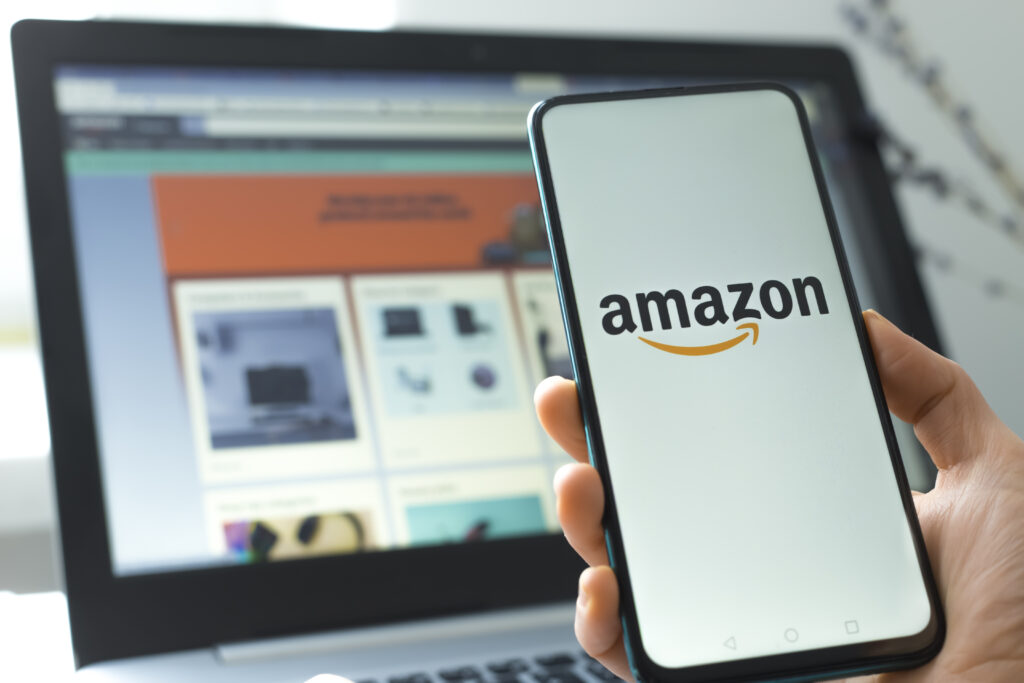 Amazon shopping app open on a smartphone in front of an online store displayed on a laptop.